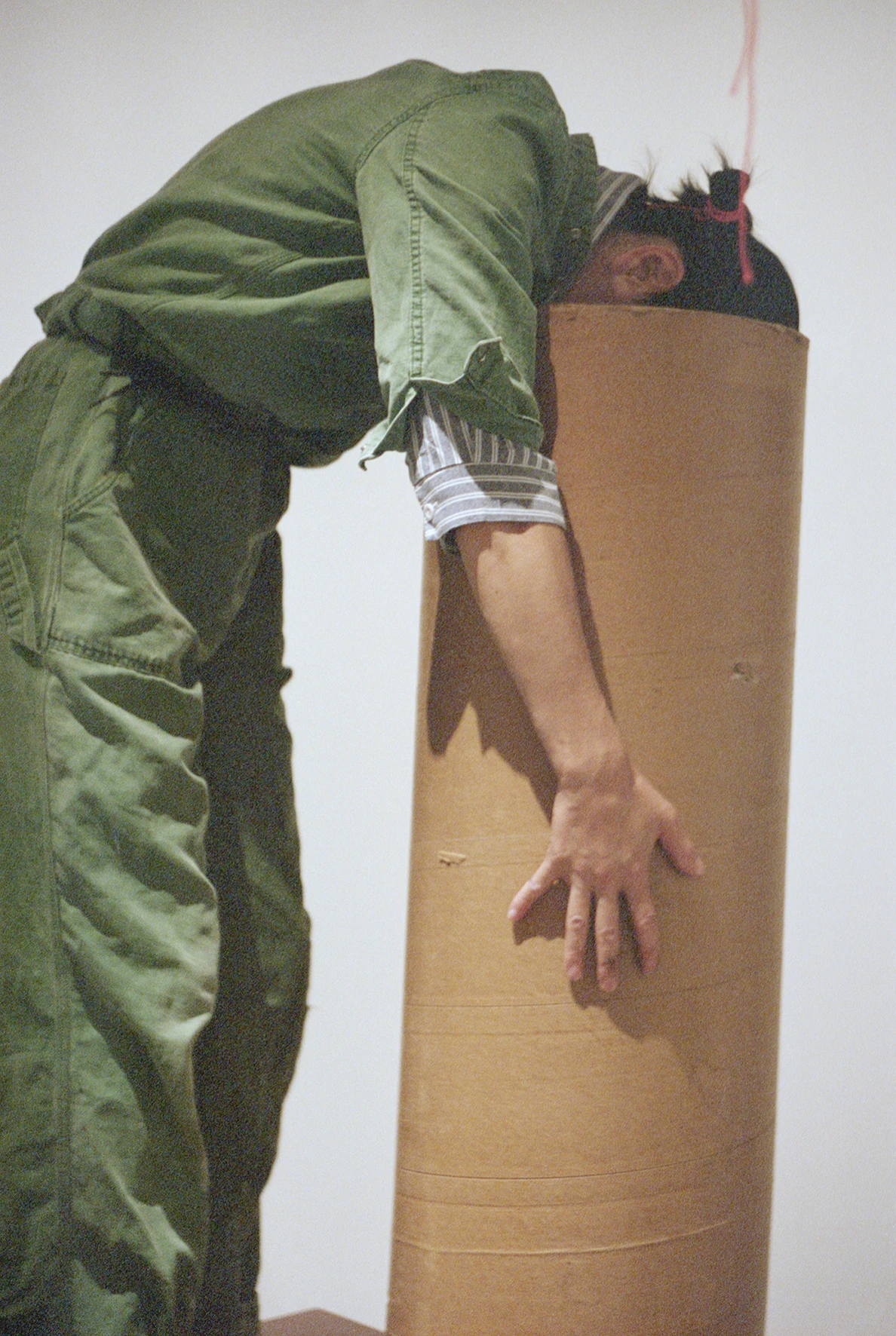 Aki Sasamoto performing Strange Attractors 2010, figure in green jumpsuit bent over large cardboard tube, MoCA Tokyo 2025