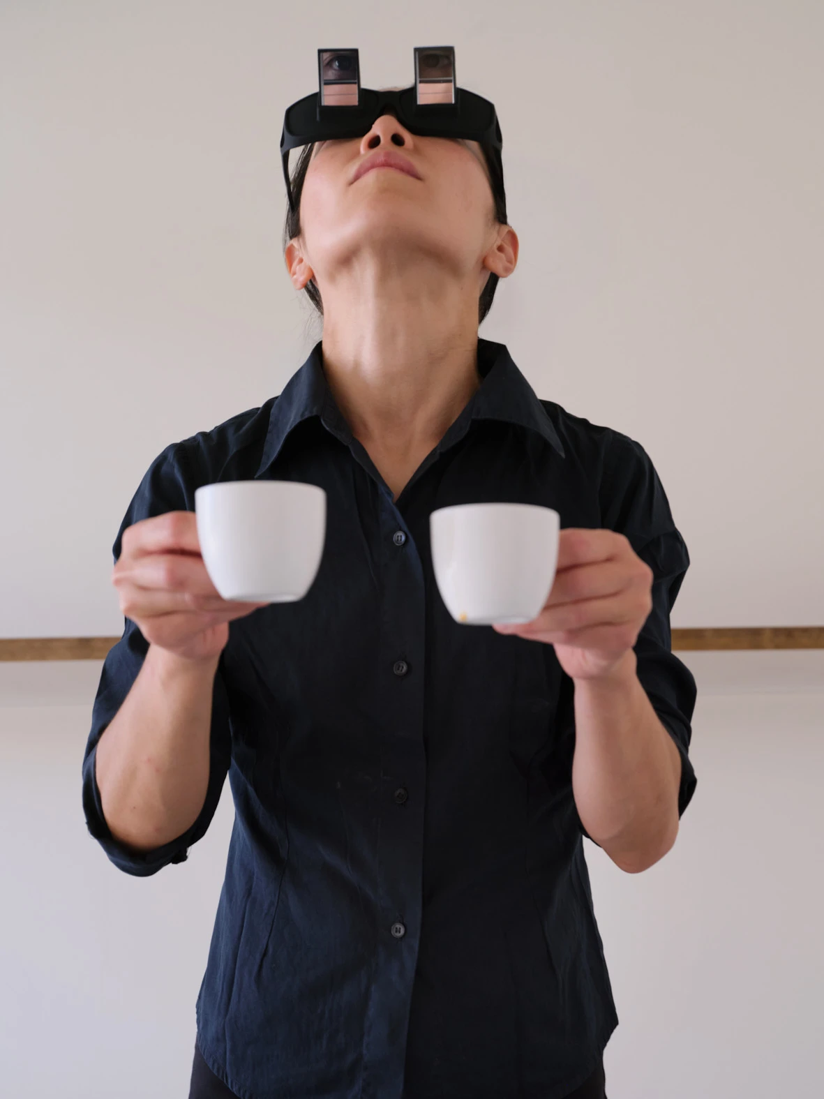 Aki Sasamoto performs Wrong Happy Hour holding two white cups wearing prism glasses, head tilted back in Milan gallery.
