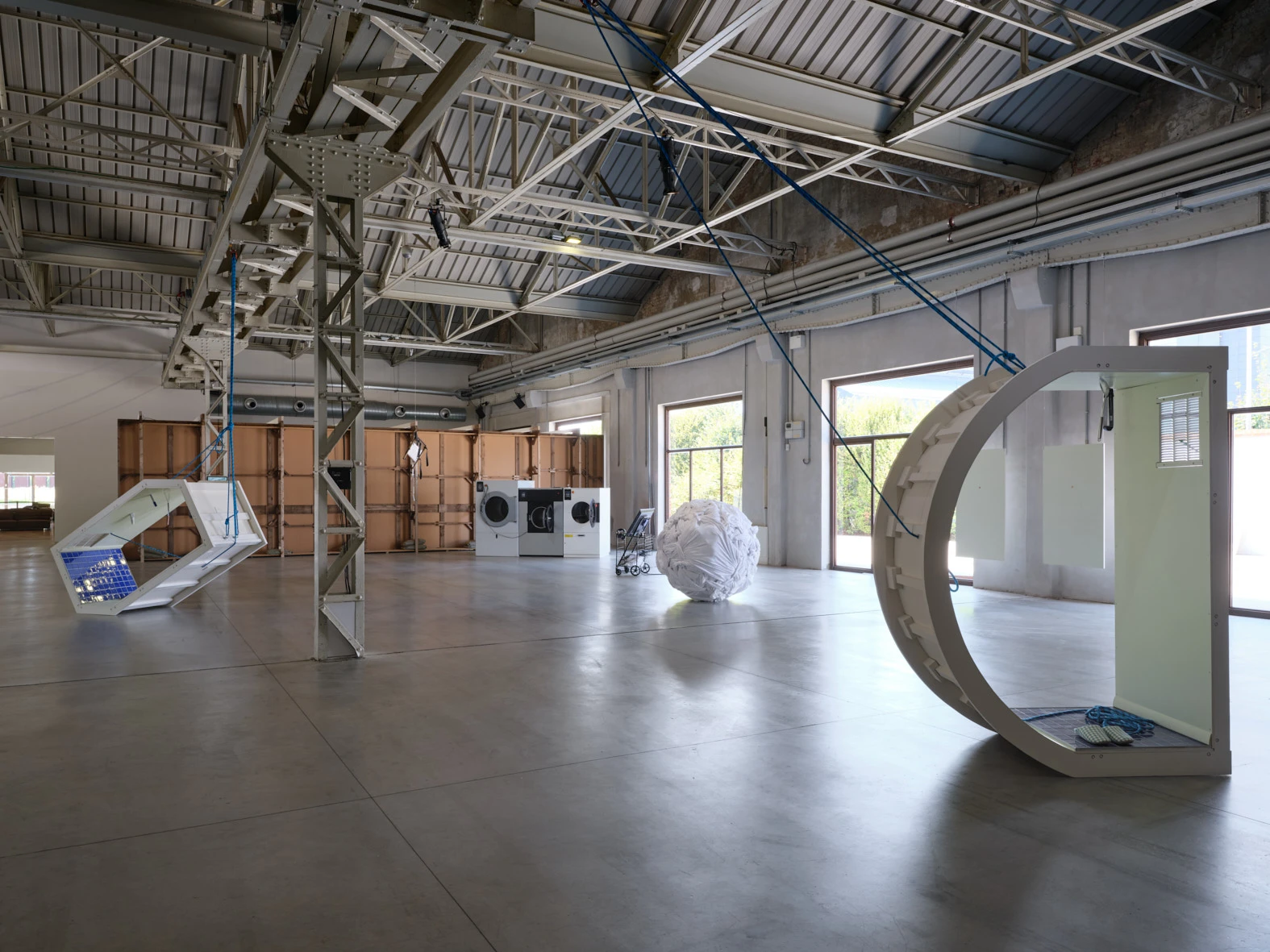 Aki Sasamoto Delicate Cycle installation view at Pirelli HangarBicocca Milan, featuring suspended frames, washing machines, and sculptural sphere