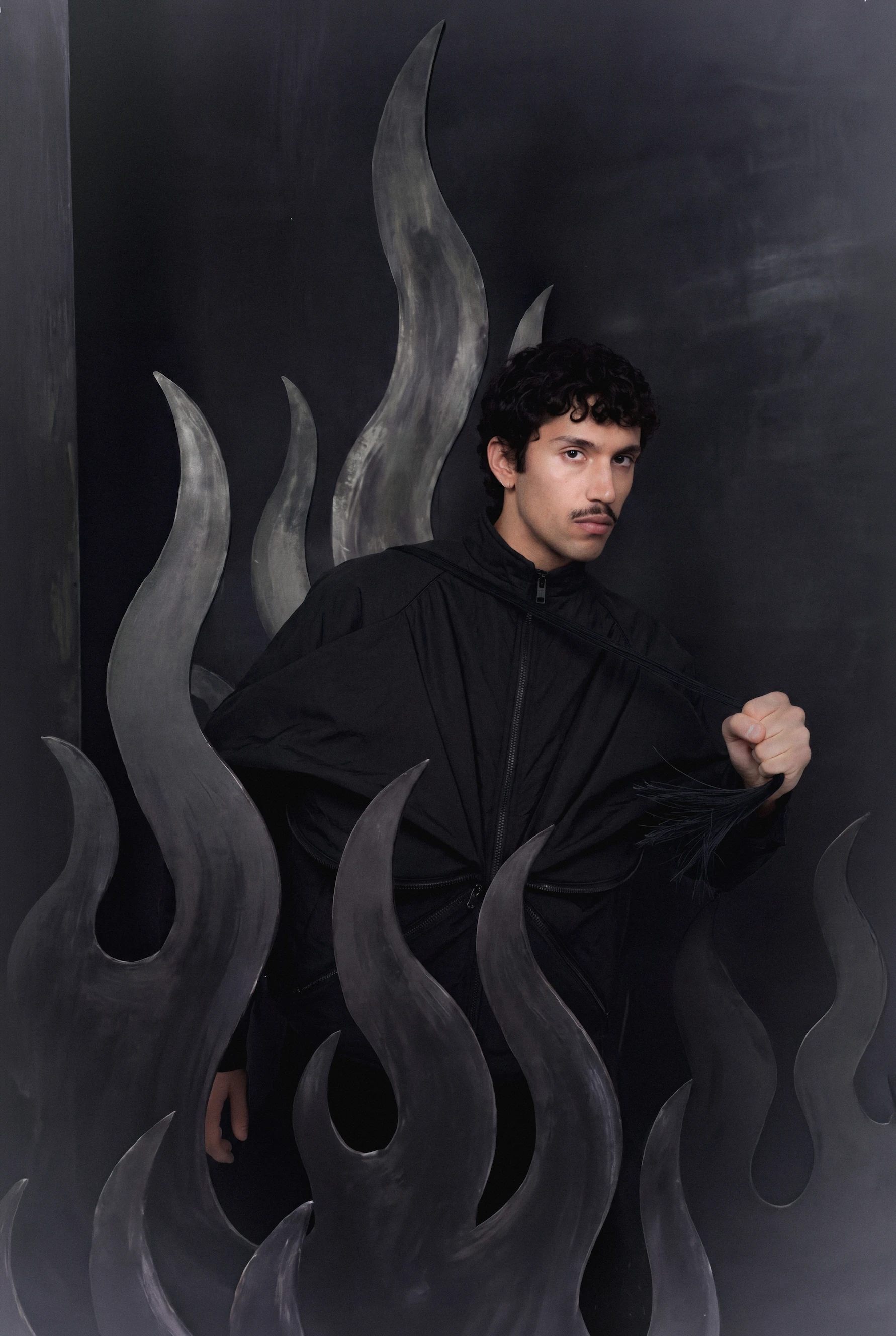Goksenin Ay wearing all-black ensemble amid painted grey flames, from debut collection Lament