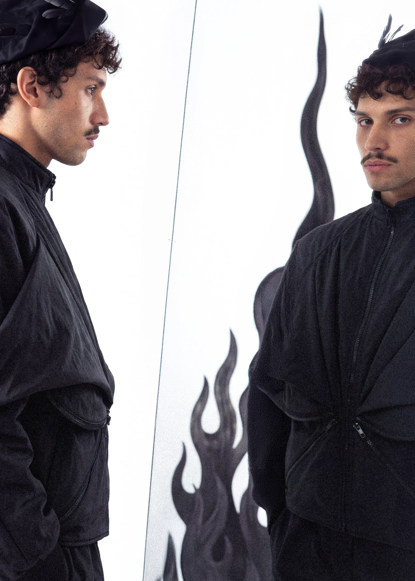 Goksenin Ay in all-black structured jacket facing mirror, flame motifs behind, from debut collection Lament