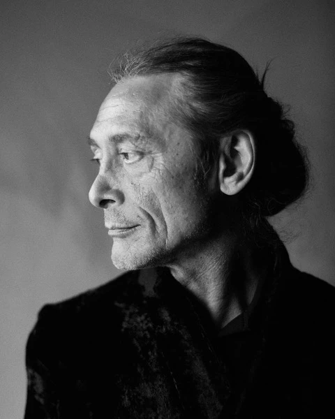 Giulio Sapio in dramatic black and white profile portrait, hair pulled back, wearing dark velvet jacket