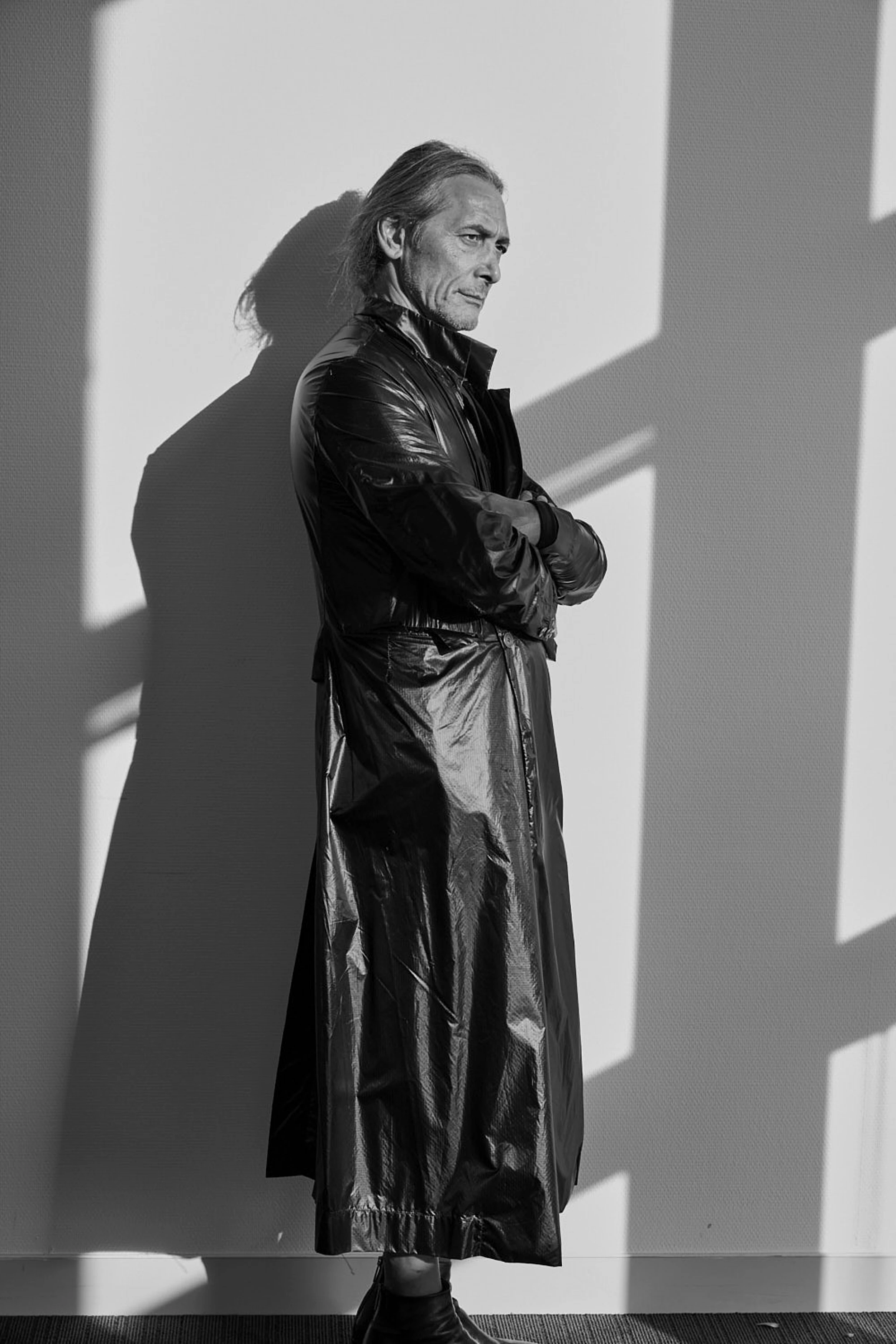 Giulio Sapio in a long black leather coat, arms crossed, dramatic shadow, SAPIO SS25 collection