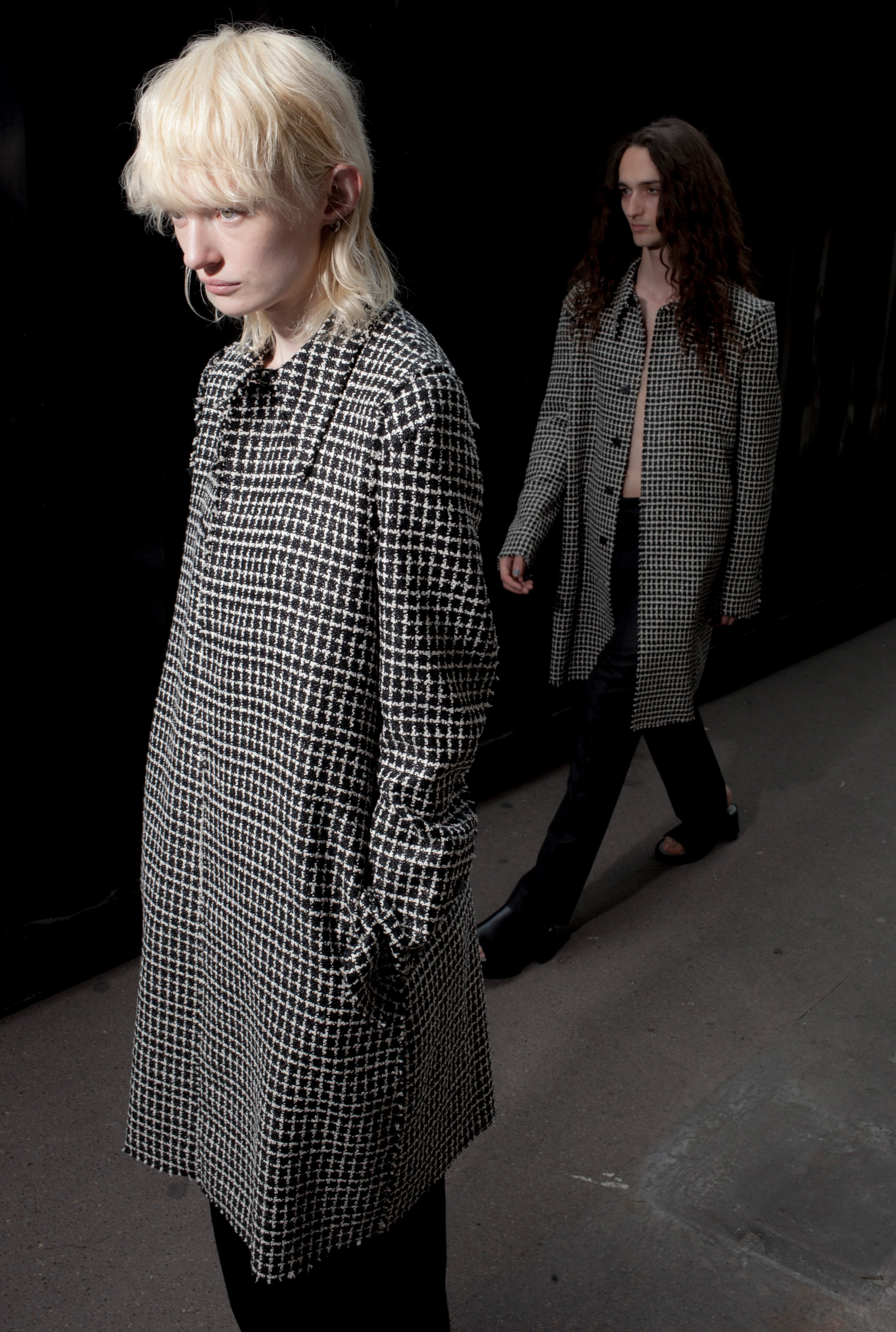 SAPIO SS24 models wearing black and white houndstooth check coats on darkened runway
