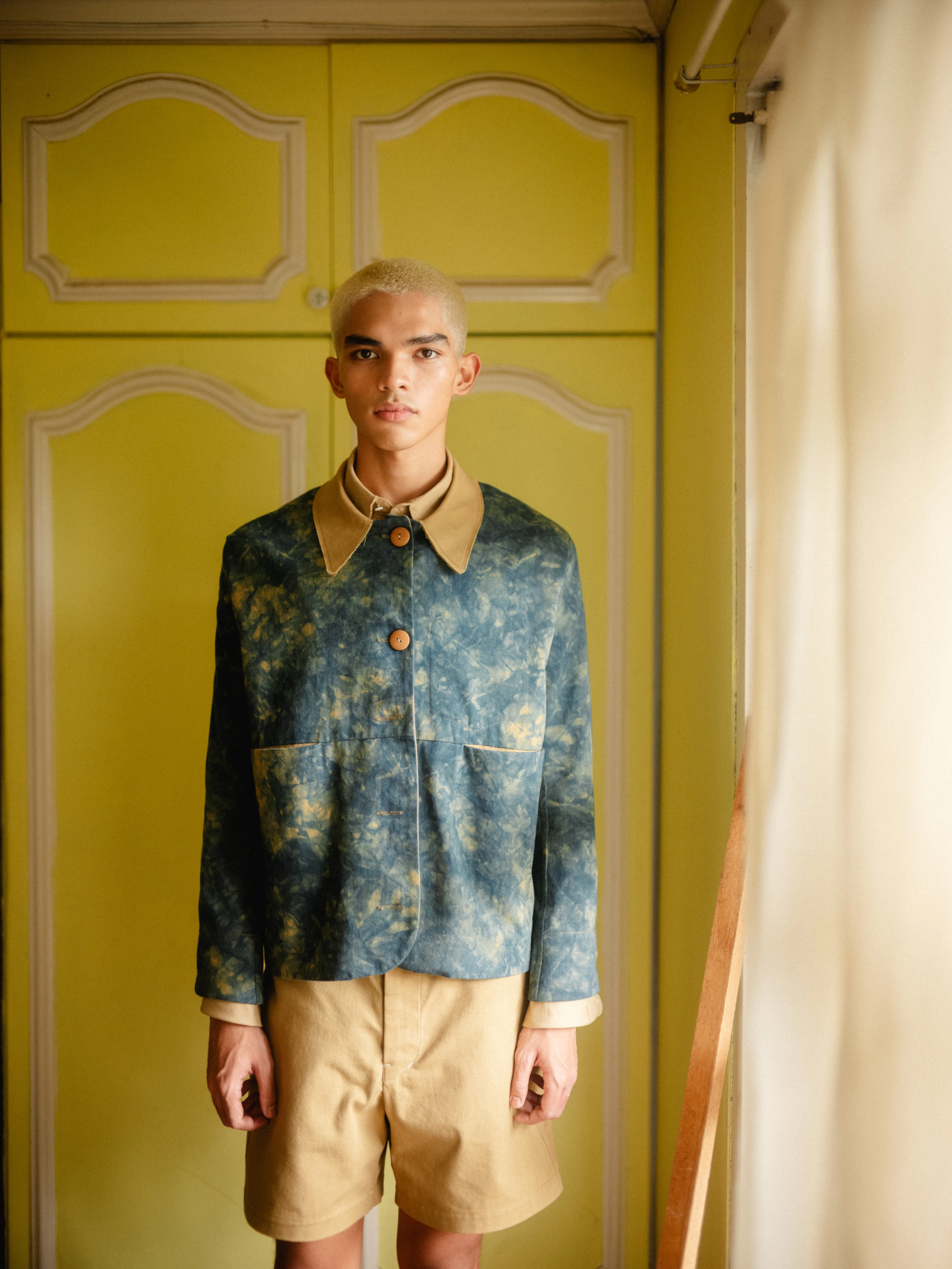 BAGASAO bleached denim jacket with tan collar, khaki shorts, styled against chartreuse paneled doors